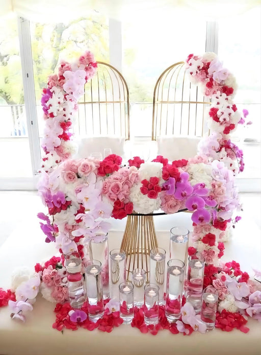 Decorative floral arch with pink and white flowers and candles on a table.