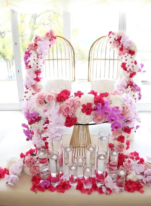 Decorative floral arch with pink and white flowers and candles on a table.